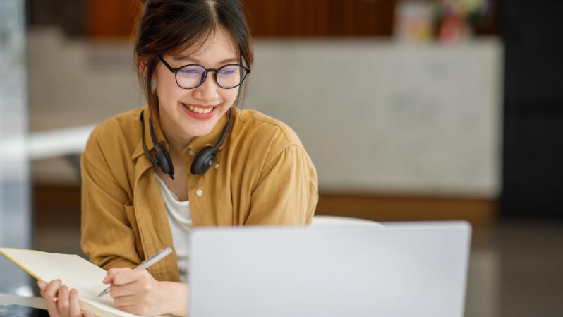 Asian woman taking a self-paced training course with laptop and a notebook