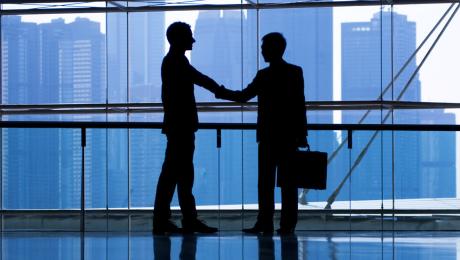 Two businessmen shaking hands in front of a large window with view of downtown.